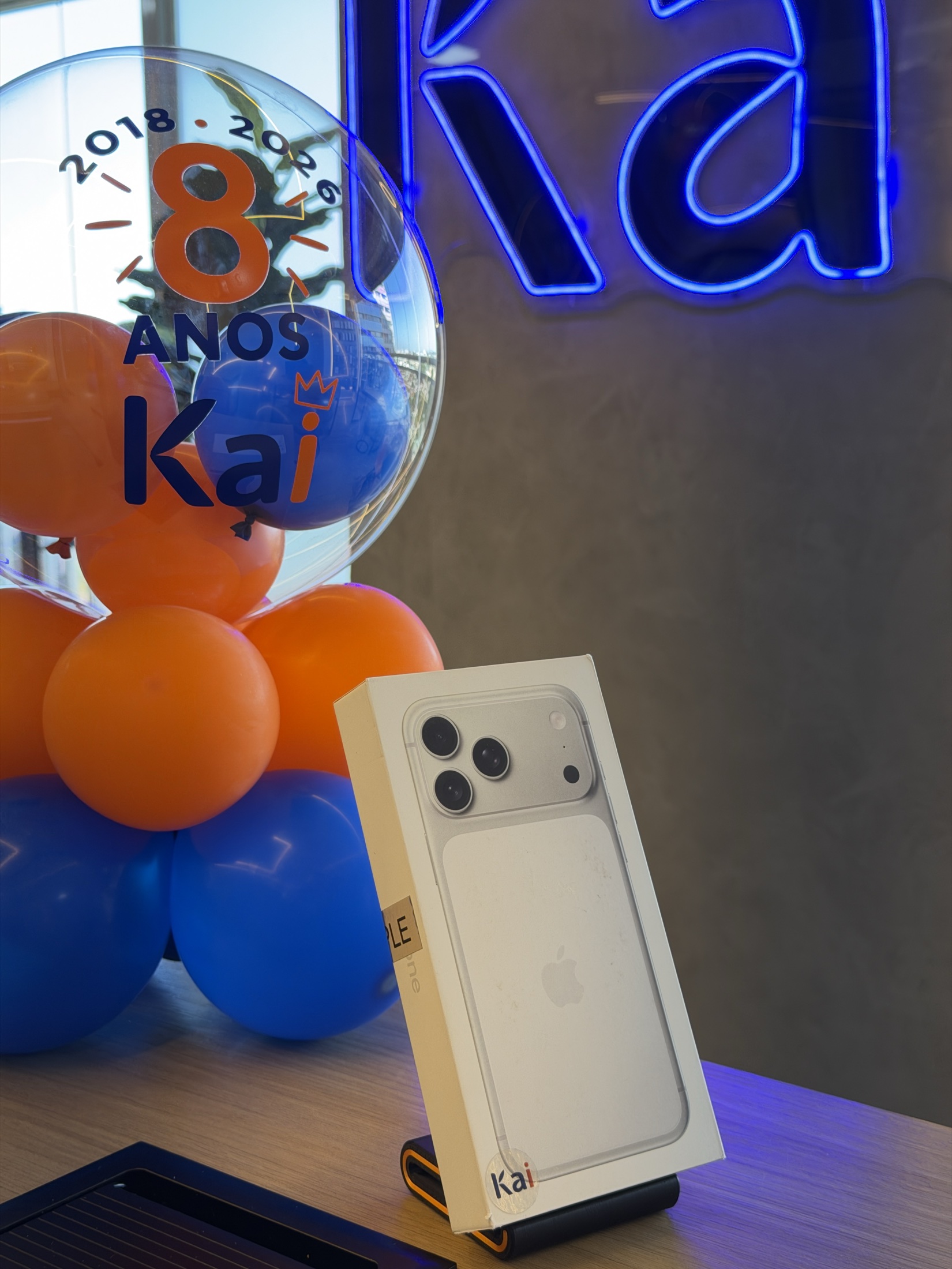 iPhone exposto ao lado dos balões azuis e laranjas de 8 anos da Kai